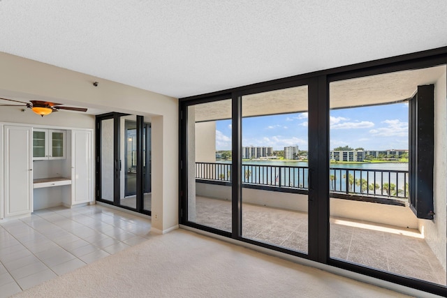 tiled empty room with a textured ceiling, a water view, a healthy amount of sunlight, and ceiling fan