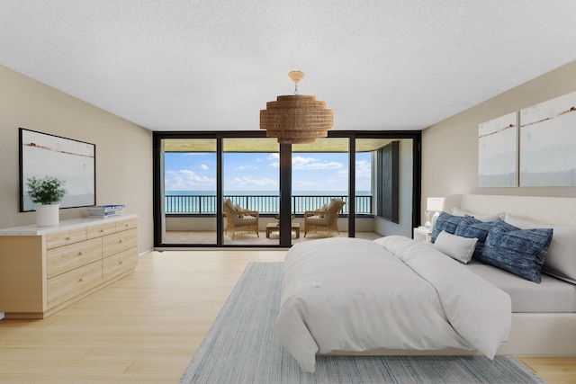 bedroom with a textured ceiling, light hardwood / wood-style flooring, access to exterior, and floor to ceiling windows