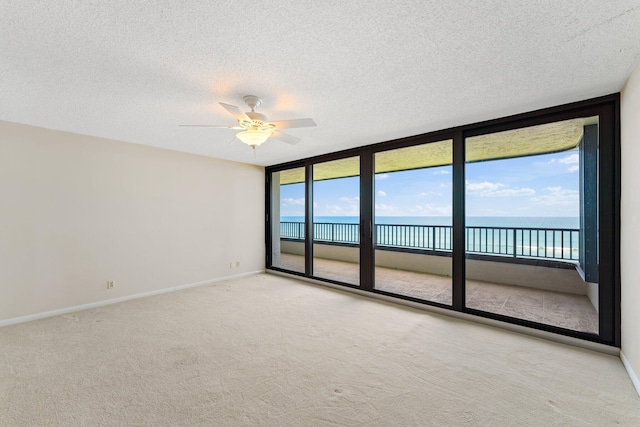 carpeted empty room featuring a textured ceiling, ceiling fan, a water view, and plenty of natural light