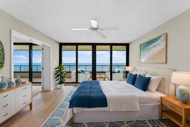 bedroom featuring light hardwood / wood-style floors, a textured ceiling, access to exterior, and a water view