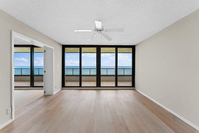 spare room with ceiling fan, a textured ceiling, light wood-type flooring, a wall of windows, and a water view