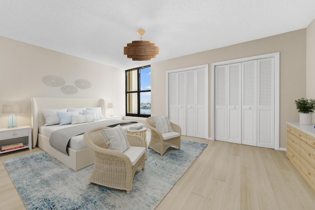 bedroom with a textured ceiling, multiple closets, and light hardwood / wood-style flooring