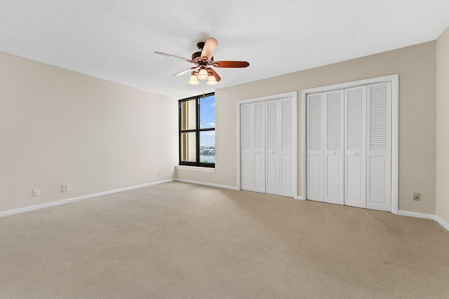 unfurnished bedroom with ceiling fan, light carpet, a textured ceiling, and two closets