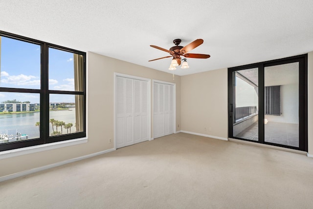 unfurnished bedroom with a textured ceiling, multiple closets, a water view, and ceiling fan