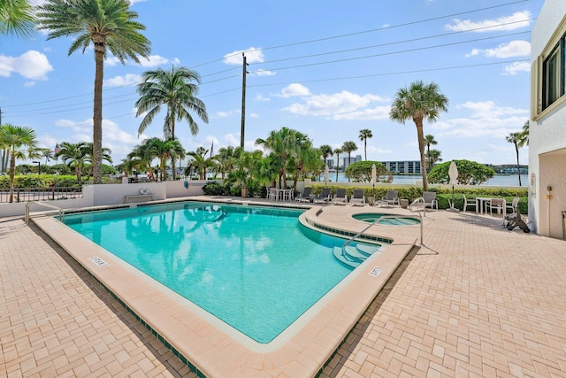 view of pool featuring a water view, a patio area, and a hot tub