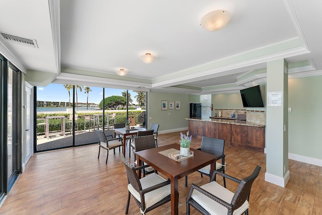 dining space with crown molding, a tray ceiling, light hardwood / wood-style floors, and a water view