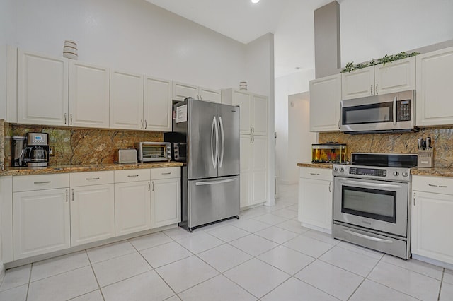 kitchen featuring white cabinets, stainless steel appliances, a towering ceiling, and light tile patterned floors