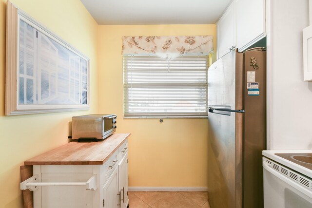 kitchen with white cabinets, light tile patterned floors, stainless steel refrigerator, white range oven, and butcher block countertops