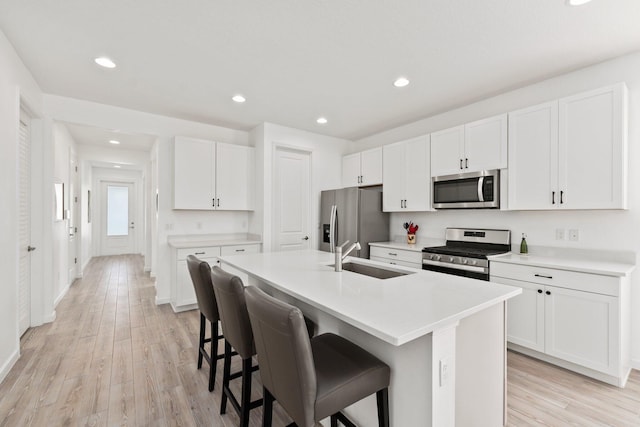 kitchen featuring a center island with sink, white cabinets, stainless steel appliances, and light wood-type flooring