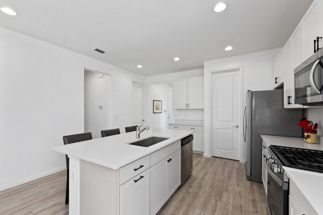 kitchen with a kitchen bar, light hardwood / wood-style floors, stainless steel appliances, white cabinets, and a center island with sink