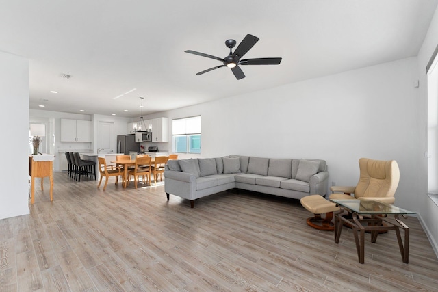 living room featuring light hardwood / wood-style floors and ceiling fan with notable chandelier