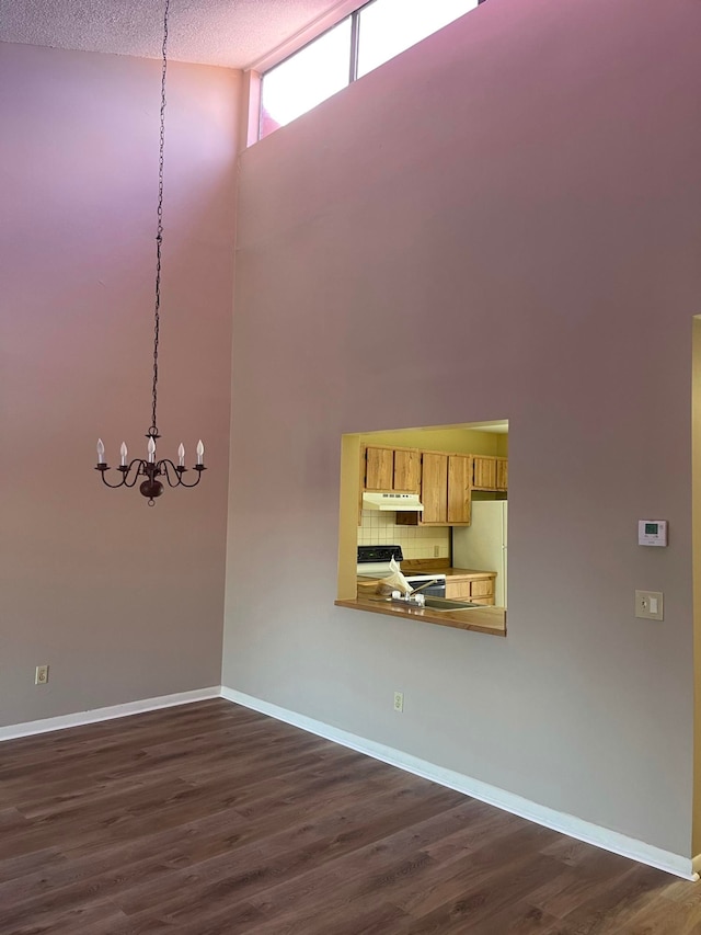 unfurnished dining area featuring dark wood-type flooring, a notable chandelier, a textured ceiling, and high vaulted ceiling