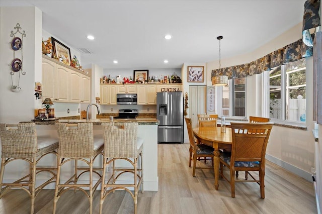 kitchen featuring light hardwood / wood-style flooring, hanging light fixtures, kitchen peninsula, dark stone countertops, and appliances with stainless steel finishes