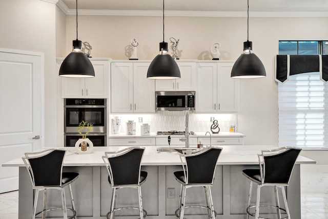 kitchen featuring appliances with stainless steel finishes, an island with sink, decorative light fixtures, white cabinets, and light stone counters