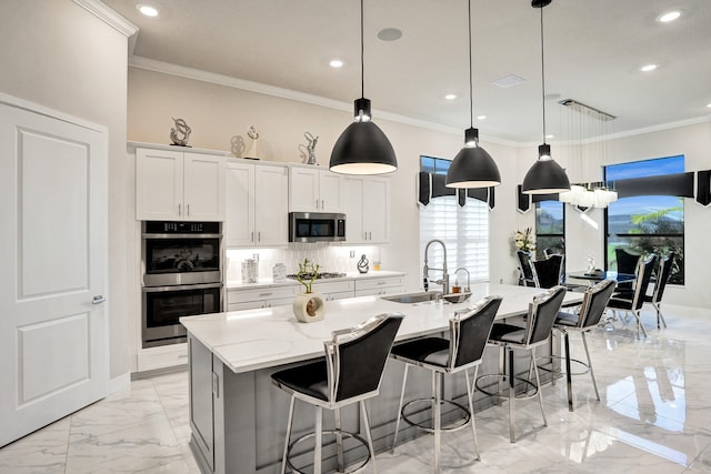 kitchen with an island with sink, stainless steel appliances, sink, pendant lighting, and white cabinets