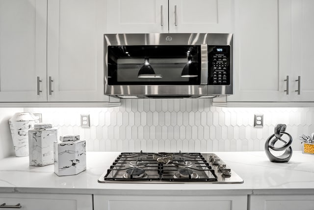 kitchen featuring light stone countertops, white cabinets, and gas cooktop