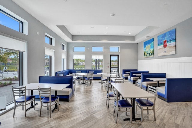 dining room featuring light wood-type flooring, a raised ceiling, a high ceiling, and plenty of natural light