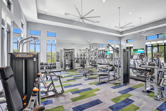 gym featuring ceiling fan, a raised ceiling, a high ceiling, and plenty of natural light