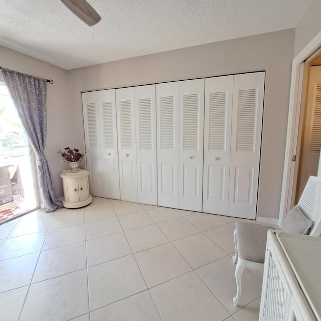 unfurnished bedroom with light tile patterned flooring, ceiling fan, a textured ceiling, and a closet