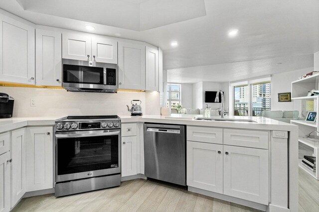 kitchen with light hardwood / wood-style floors, appliances with stainless steel finishes, sink, and white cabinets