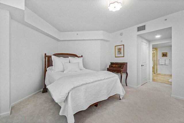 bedroom featuring light carpet, a textured ceiling, and ensuite bath