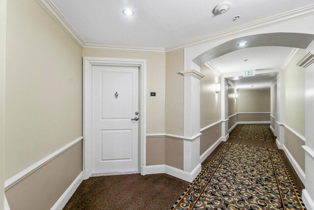 corridor with dark carpet, crown molding, ornate columns, and a textured ceiling