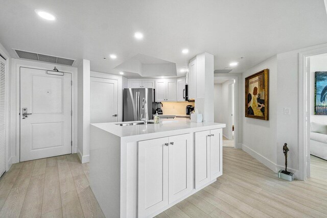 kitchen featuring a center island with sink, stainless steel fridge, white cabinets, and light hardwood / wood-style flooring