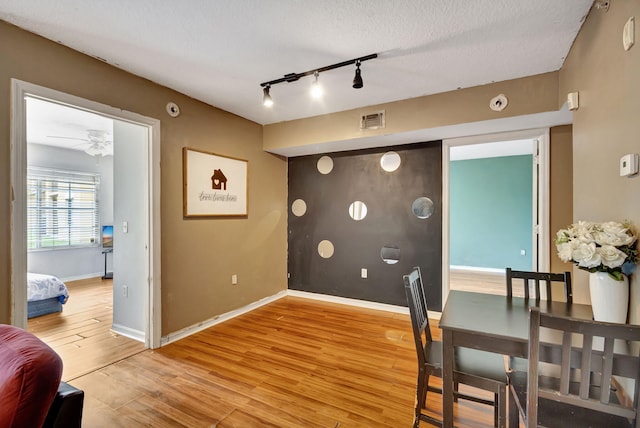 dining room with light hardwood / wood-style floors, a textured ceiling, rail lighting, and ceiling fan