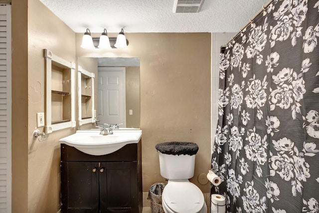 bathroom with toilet, a textured ceiling, walk in shower, and vanity