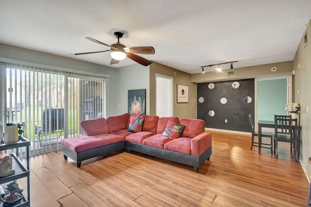 living room featuring rail lighting, ceiling fan, a textured ceiling, and light wood-type flooring