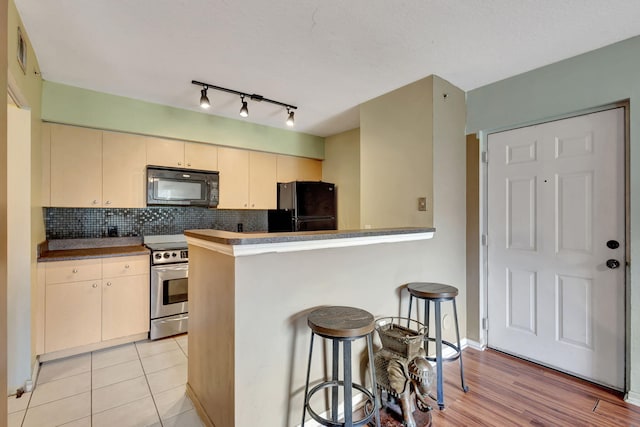 kitchen featuring light wood-type flooring, black appliances, a breakfast bar area, and kitchen peninsula