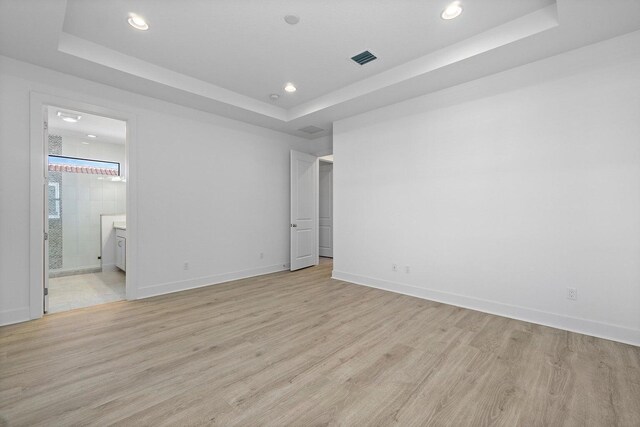 unfurnished bedroom featuring light hardwood / wood-style flooring, ensuite bath, and a tray ceiling