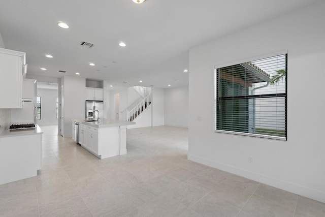 kitchen with an island with sink, stainless steel fridge with ice dispenser, white cabinetry, and light tile patterned floors