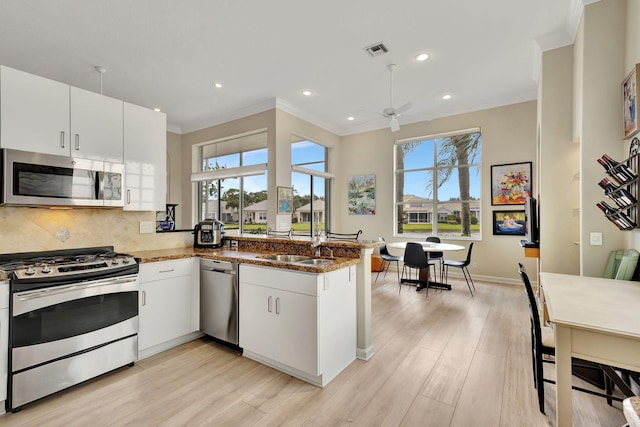 kitchen with appliances with stainless steel finishes, kitchen peninsula, white cabinets, and plenty of natural light