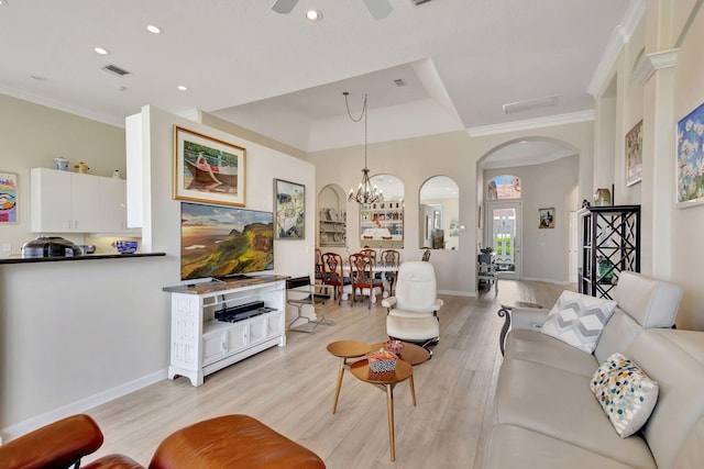 living room with a raised ceiling, light hardwood / wood-style flooring, ceiling fan with notable chandelier, and crown molding