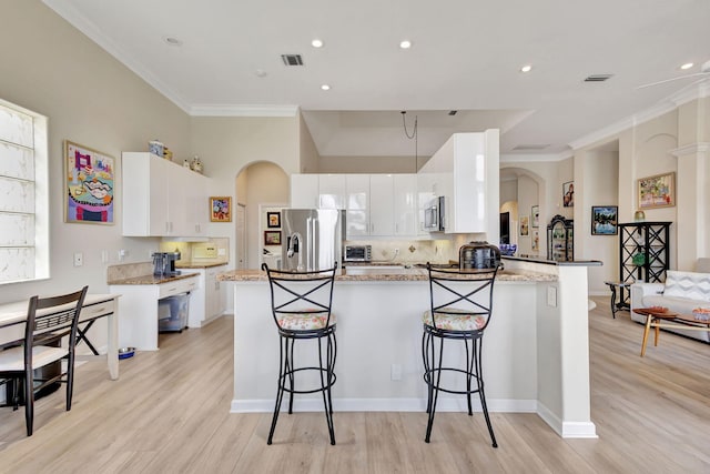 kitchen featuring a kitchen breakfast bar, white cabinetry, stainless steel appliances, and light hardwood / wood-style floors