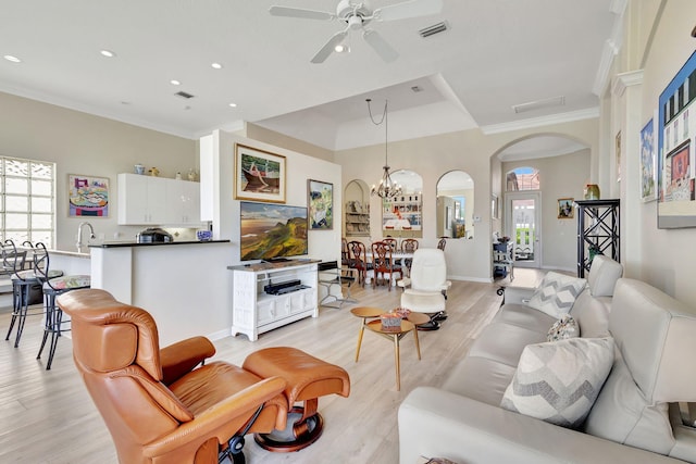 living room with sink, crown molding, ceiling fan with notable chandelier, and light wood-type flooring