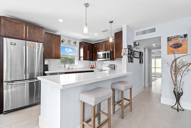 kitchen featuring a breakfast bar area, hanging light fixtures, dark brown cabinets, light wood-type flooring, and appliances with stainless steel finishes