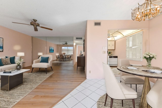 dining space with a textured ceiling, ceiling fan with notable chandelier, and light hardwood / wood-style floors