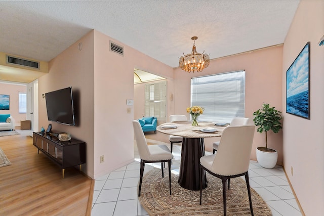 dining area featuring a notable chandelier, a textured ceiling, and light wood-type flooring