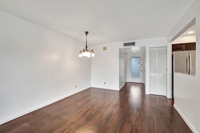 unfurnished room featuring a notable chandelier, dark hardwood / wood-style floors, and a textured ceiling