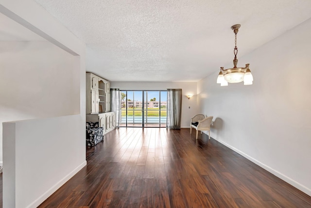 unfurnished living room featuring a textured ceiling, dark hardwood / wood-style floors, and an inviting chandelier