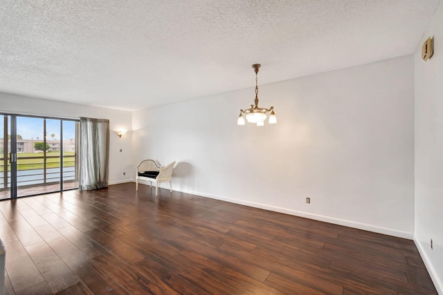 empty room with a notable chandelier, dark hardwood / wood-style floors, and a textured ceiling