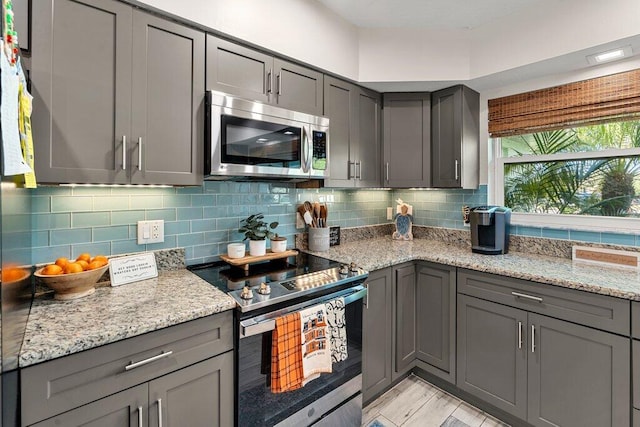 kitchen with decorative backsplash, light hardwood / wood-style flooring, stainless steel appliances, gray cabinets, and light stone counters