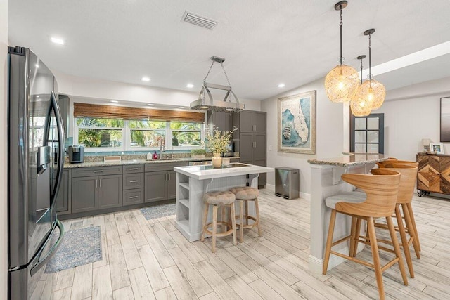 kitchen with a kitchen island, hanging light fixtures, light wood-type flooring, gray cabinets, and stainless steel refrigerator