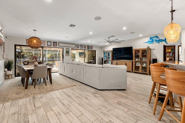 living room with ceiling fan, a textured ceiling, and light wood-type flooring