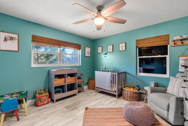 bedroom featuring a textured ceiling, a crib, light wood-type flooring, and ceiling fan