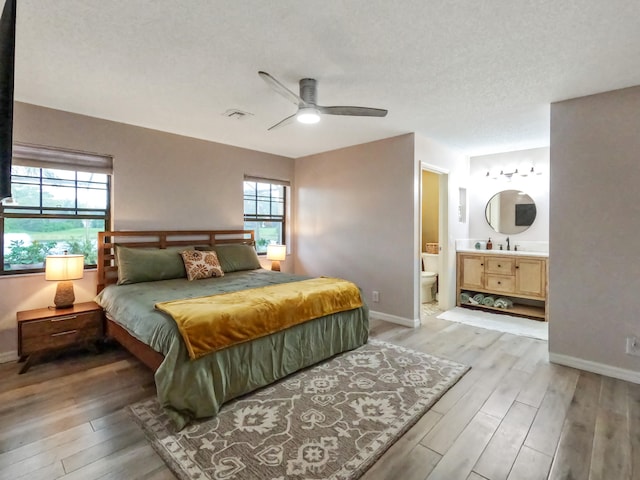 bedroom with multiple windows, ensuite bathroom, hardwood / wood-style floors, and ceiling fan