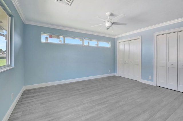 unfurnished bedroom featuring light hardwood / wood-style floors, ornamental molding, multiple closets, and ceiling fan