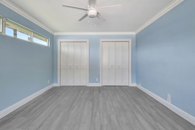 unfurnished bedroom featuring ceiling fan, crown molding, light hardwood / wood-style flooring, and two closets